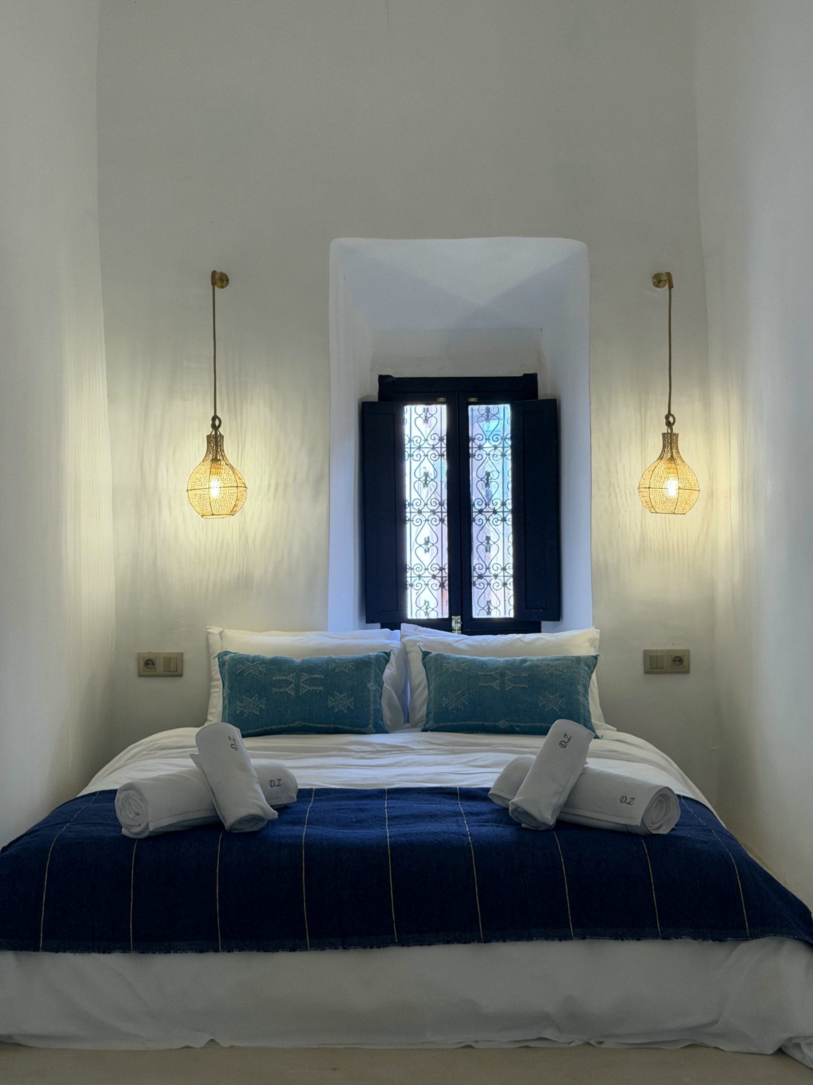 Chambre La Majorelle : lit sur estrade en tadelakt sous une fenêtre à volets bleu nuit