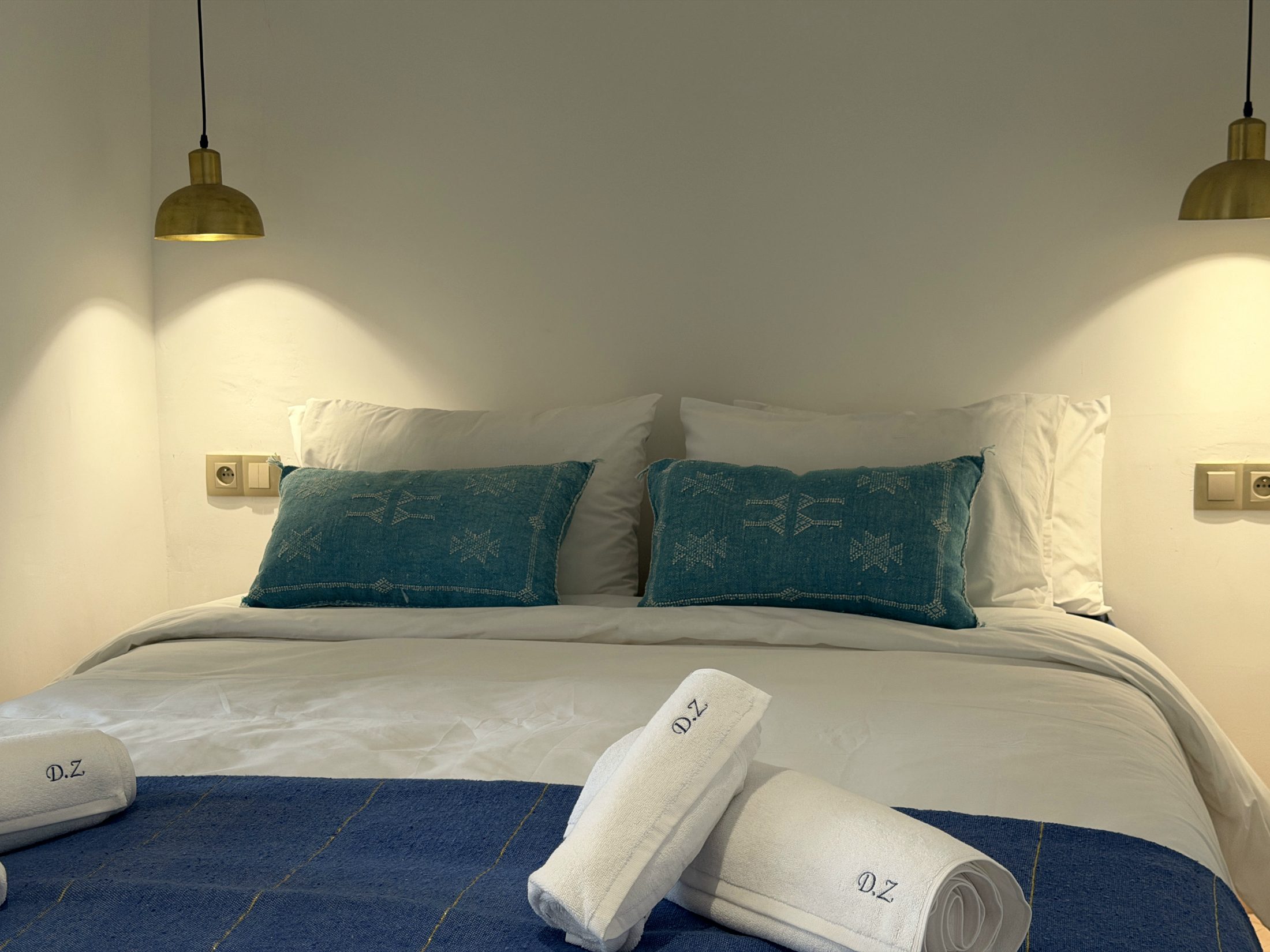 Chambre L'Alcôve : grand lit, appliques en laiton et étagère de céramiques bleues