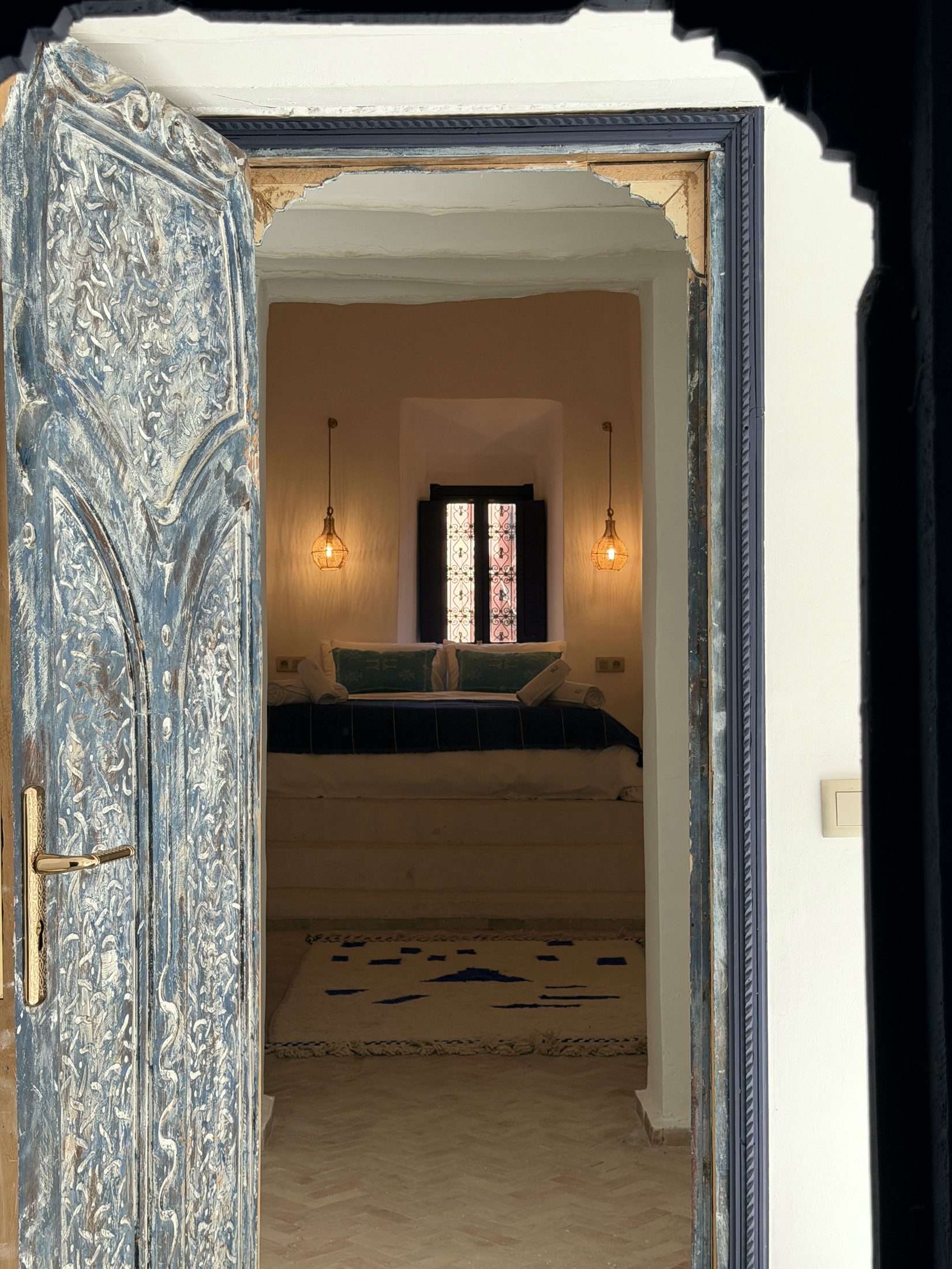 Porte ancienne sculptée et peinte en bleu ouvrant sur une chambre